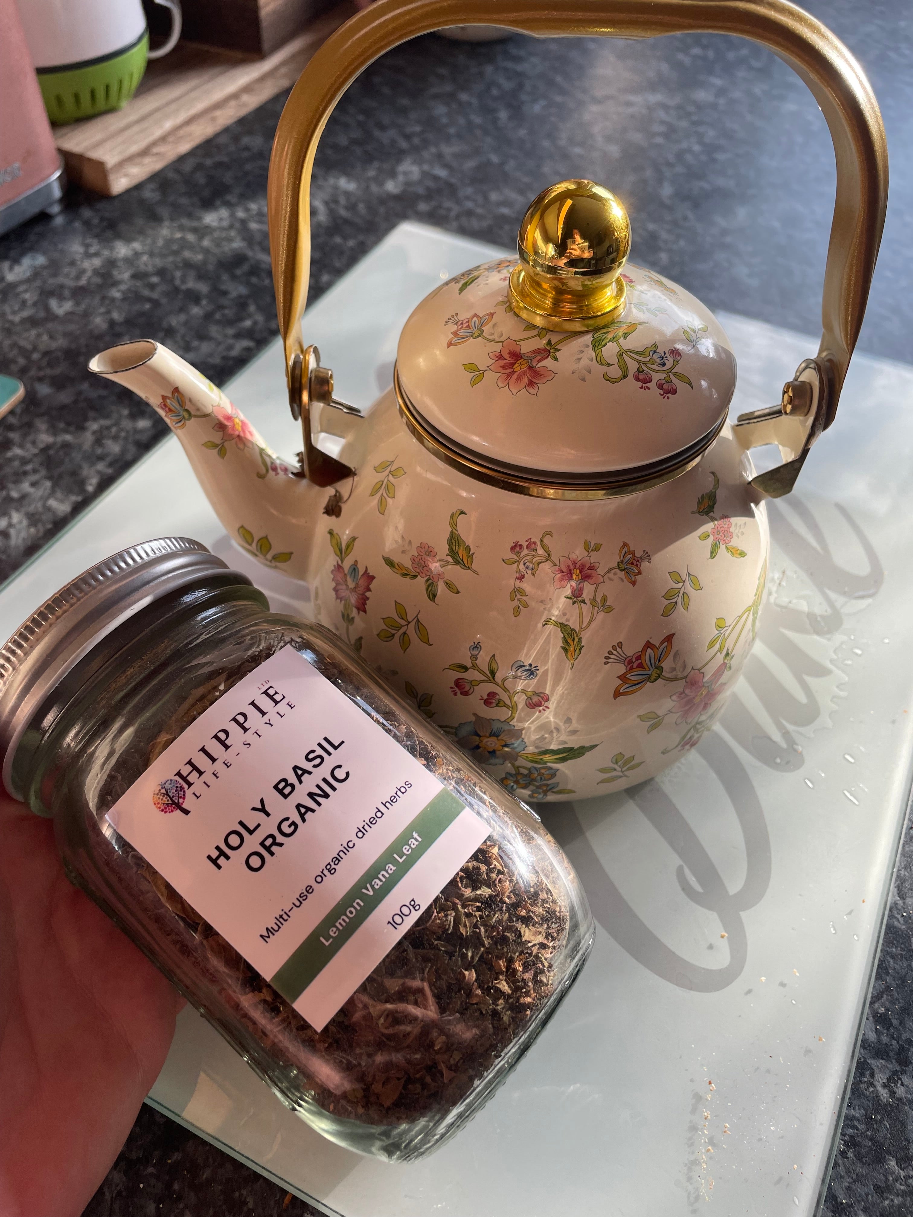 a glass jar of herbal tea pictured with a botanical floral pattern herbalist teapot in an apothecary ta shop.